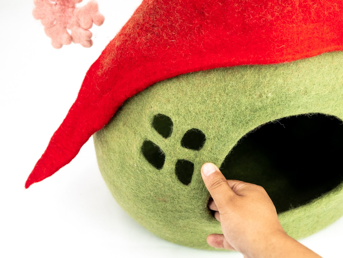 Green pet bed with red felt roof and paw prints, hand touching the entrance.