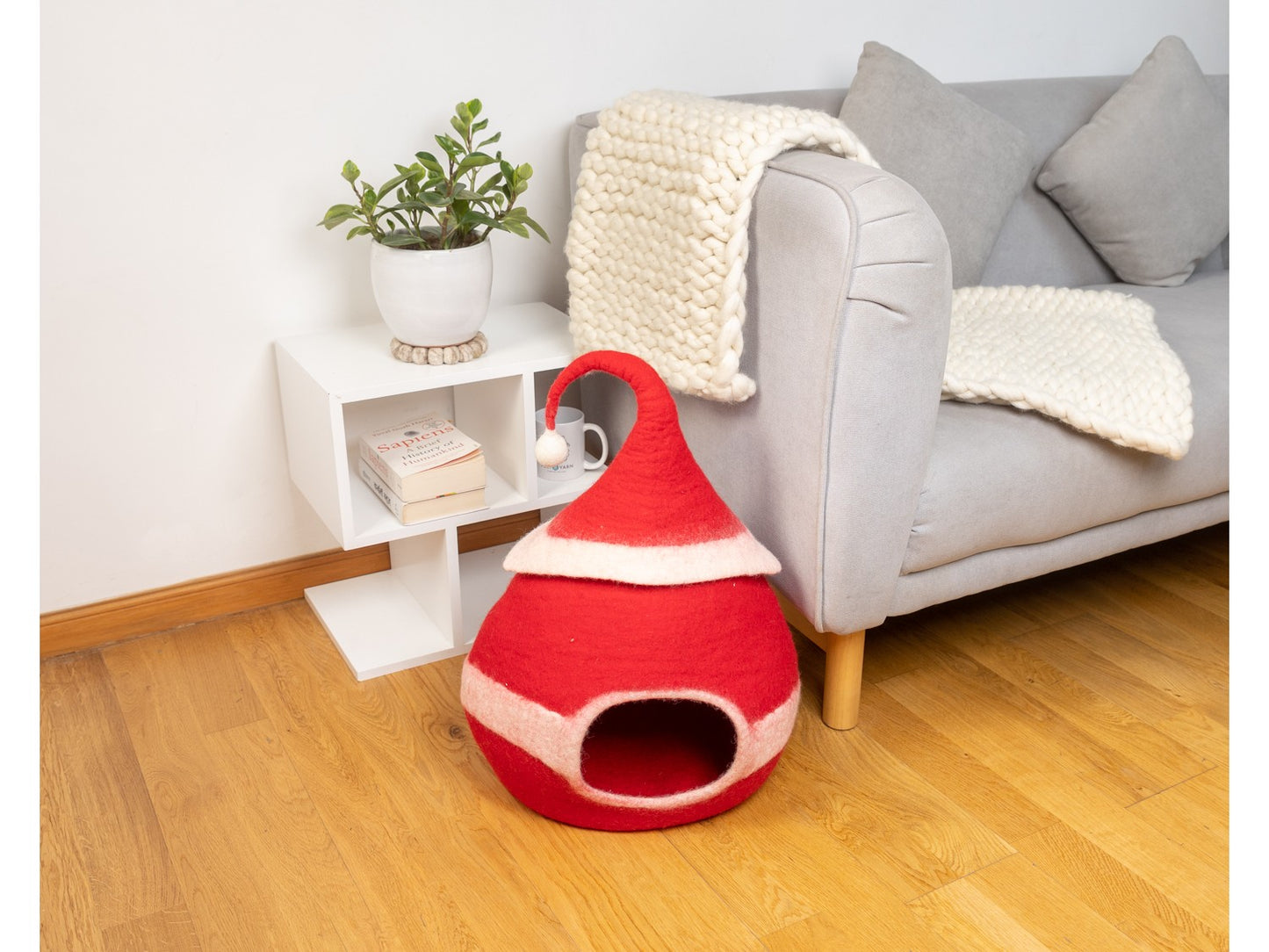 Red pet bed on a wooden floor with a gray sofa and white side table in the background.