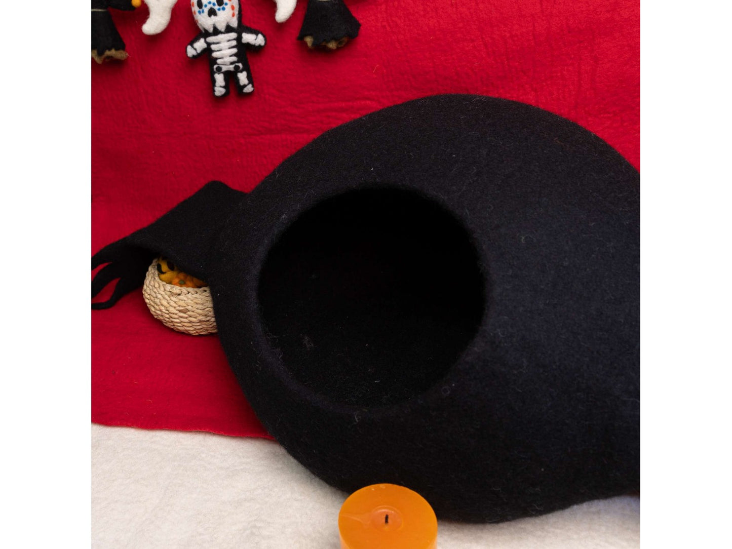 Black cat bed on a red blanket with small toys and a candle