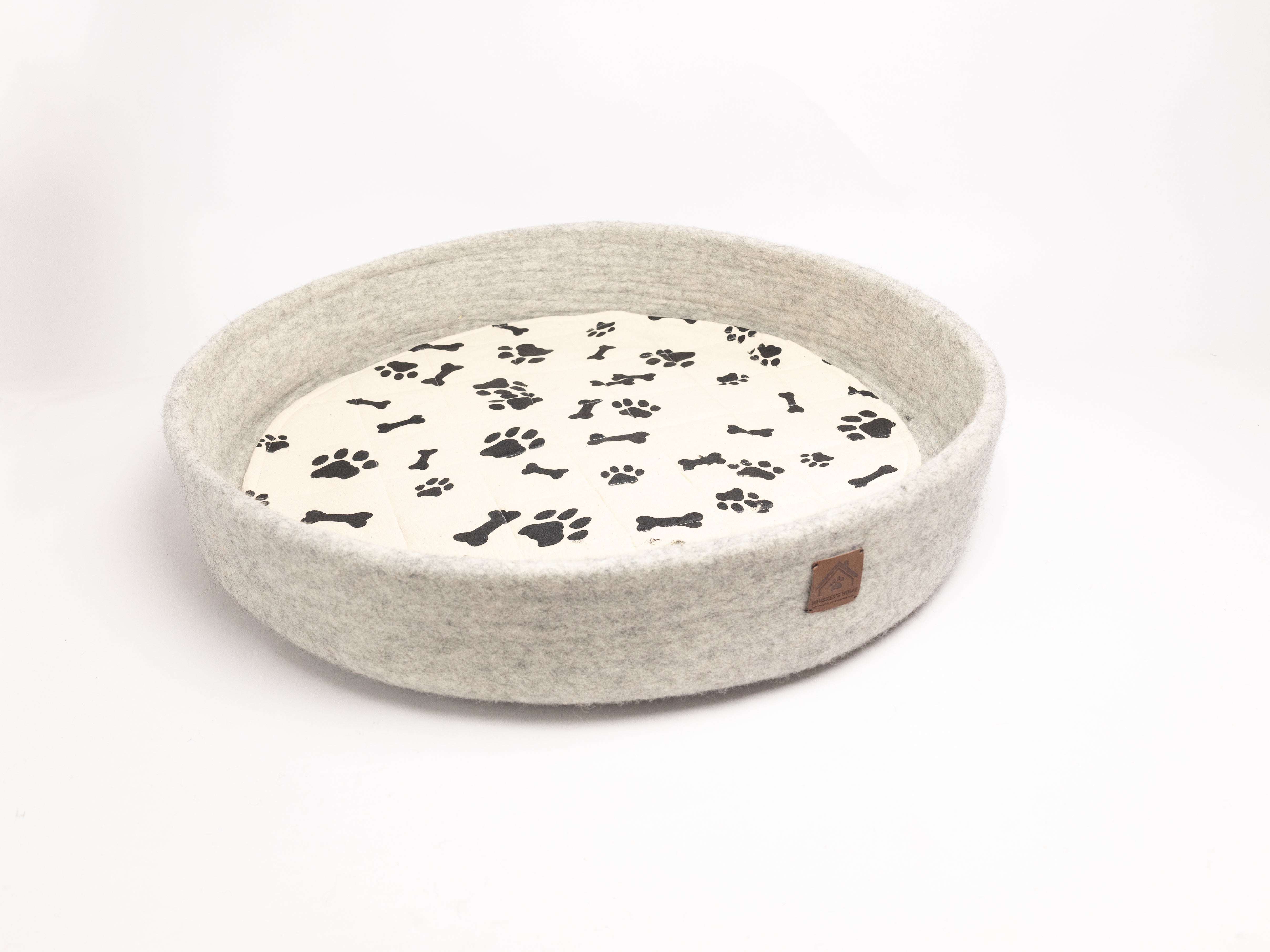 grey round felt dog bed with black paw printed patterns on white cushion from side