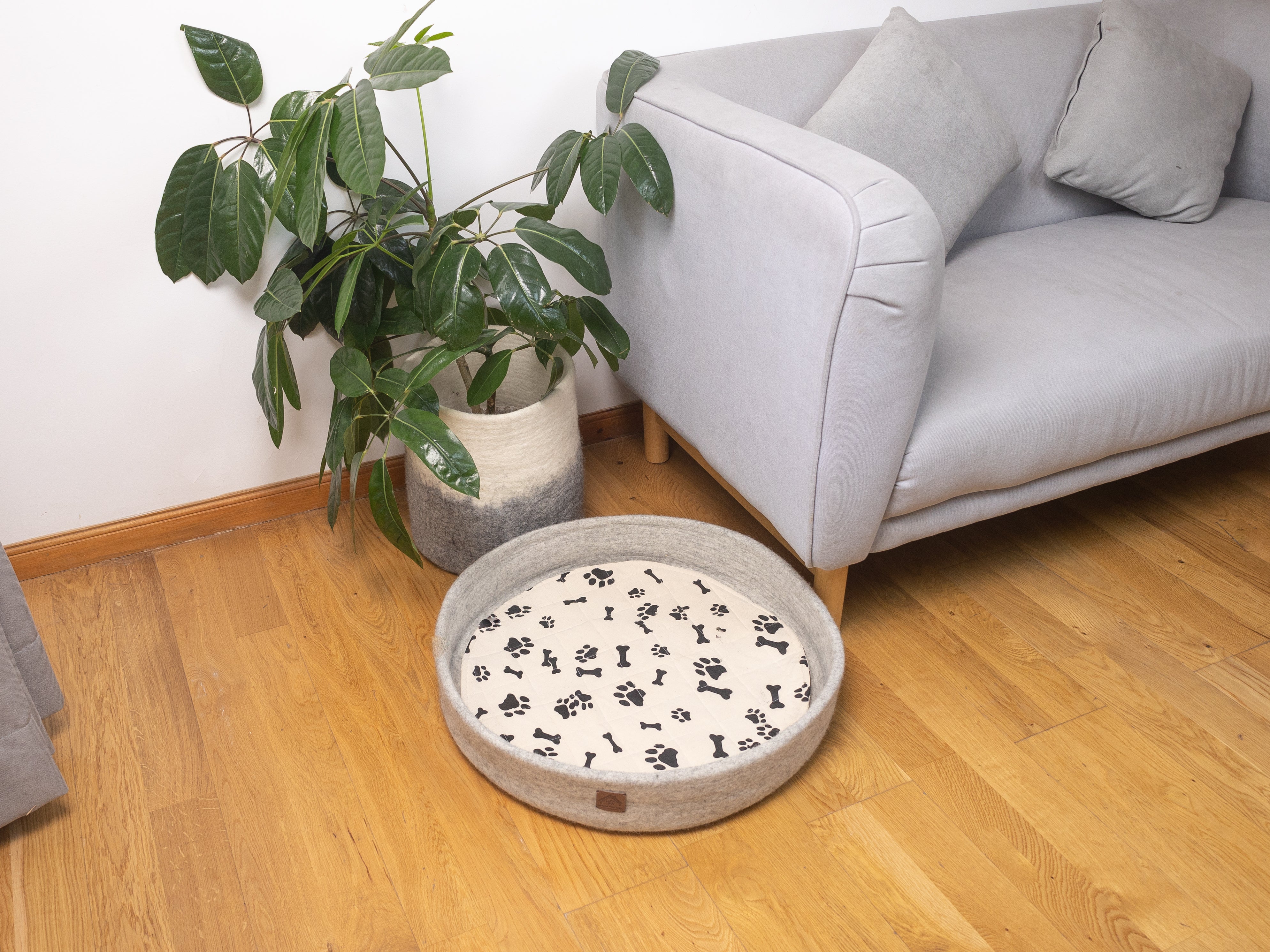 grey felted dog bed with black print paw patterns, dog bed on living floor with sofa, felt basket