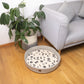 grey felted dog bed with black print paw patterns, dog bed on living floor with sofa, felt basket