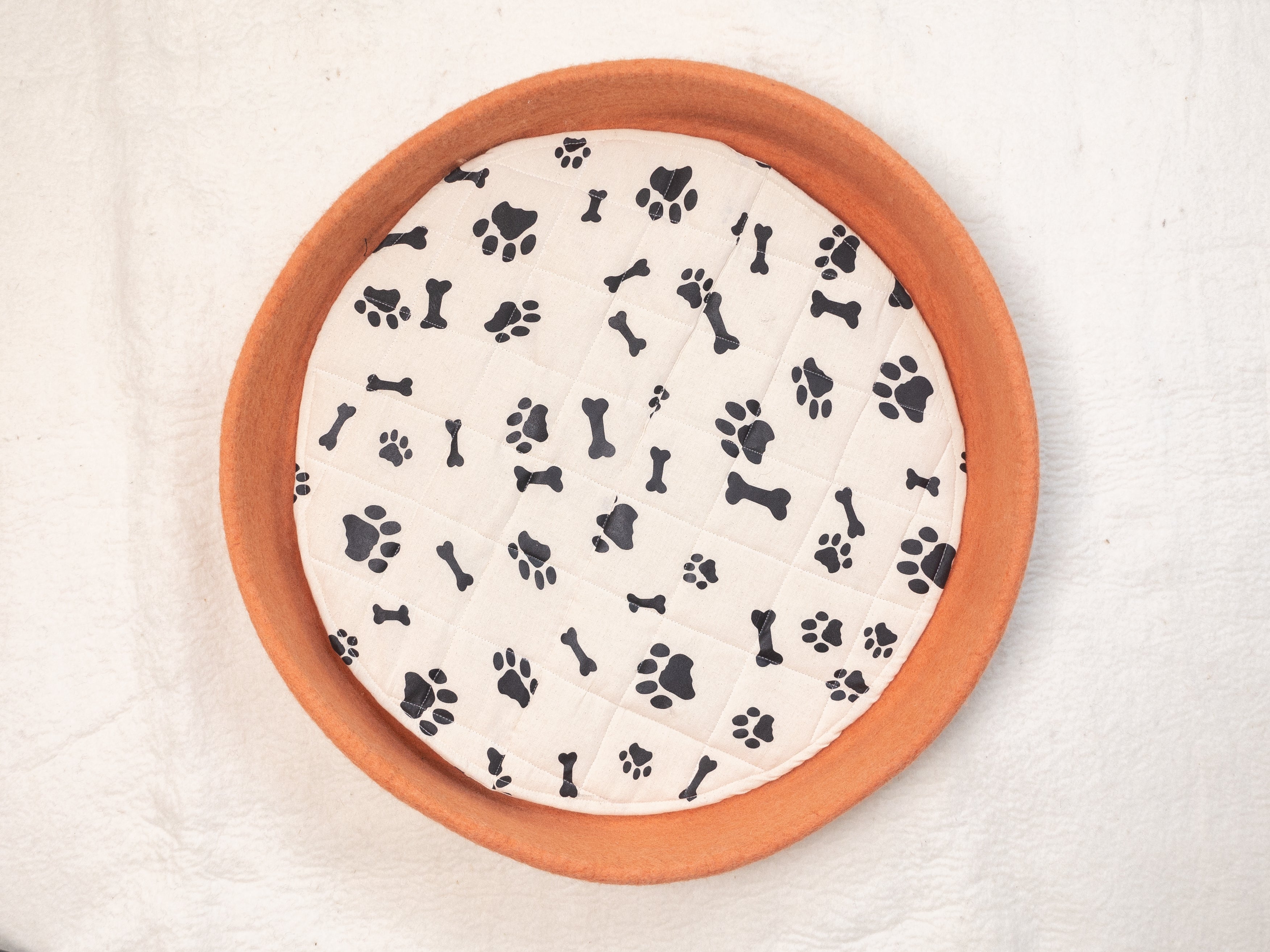 round orange felt dog bed with  paw and bones printed patterns in white cushion