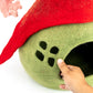 Green pet bed with red felt roof and paw prints, hand touching the entrance.