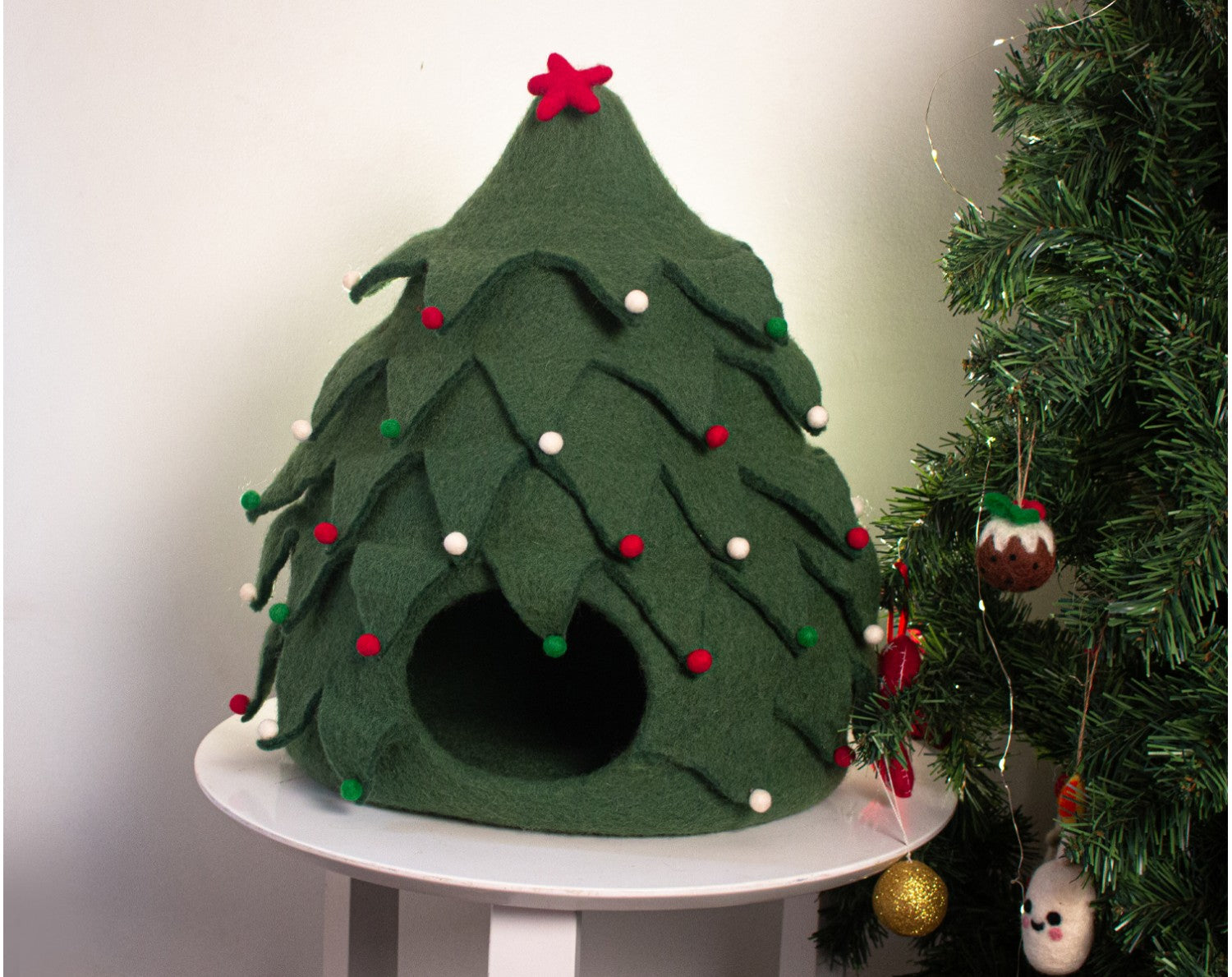 Green felt Christmas tree-shaped pet house with decorative lights and ornaments on a white surface.