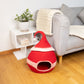 Red pet bed on a wooden floor with a gray sofa and white side table in the background.