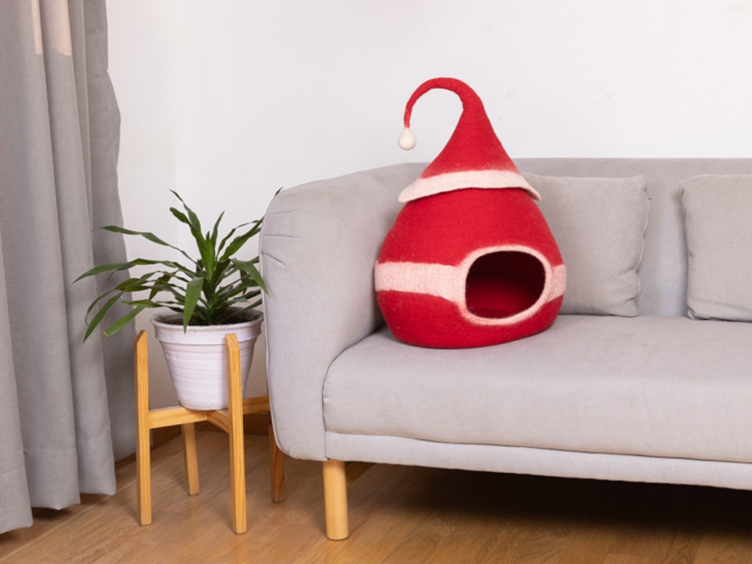 Red gnome-shaped pet bed on a light gray sofa with a plant in the background