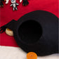 Black cat bed on a red blanket with small toys and a candle