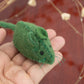 Hand holding a small green felt mouse toy against a blurred background