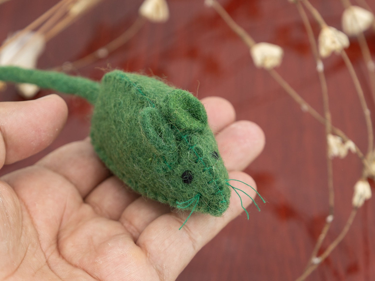 Hand holding a small green felt mouse toy against a blurred background